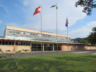 Foto da fachada frontal do prédio da reitoria da Universidade Federal de Santa Catarina À frente, há três bandeiras, da esquerda para a direita: bandeira de Santa Catarina, bandeira do Brasil e bandeira da UFSC